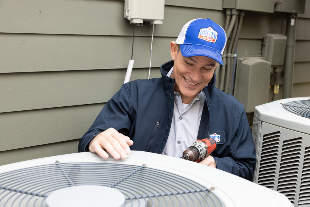Technician servicing an outdoor HVAC unit next to a home.