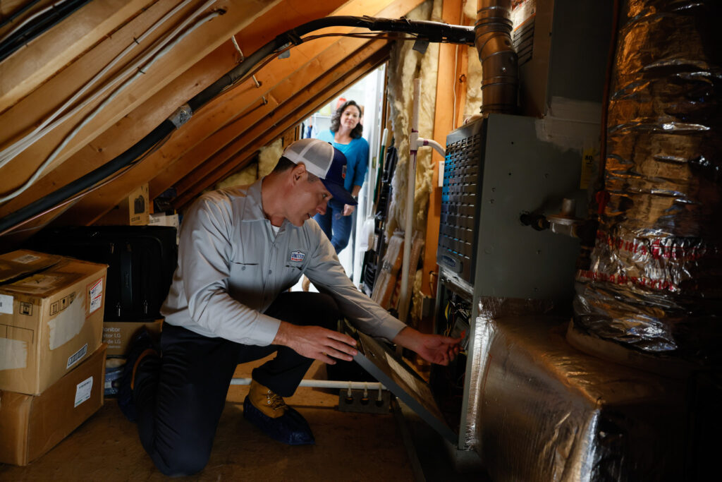 Technician replacing a furnace in a home's unfinished attic.