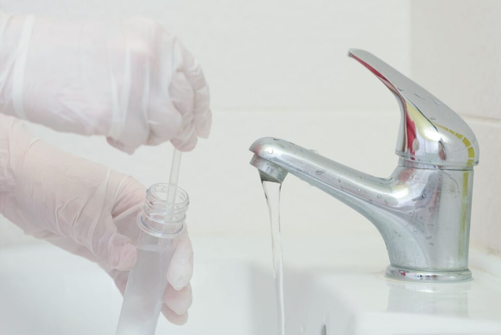Gloved hand taking a water sample from a home sink