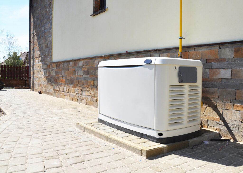 Residential standby generator installed next to a brick-and-white-stucco home.