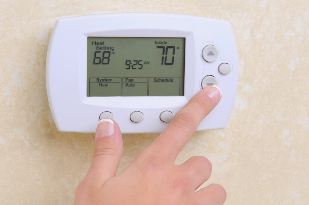 Close up of a woman's hand setting the temperature on a modern programable thermostat.