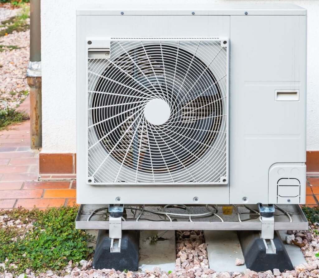Close-up of air-source heat pump installed outside a white stucco home.