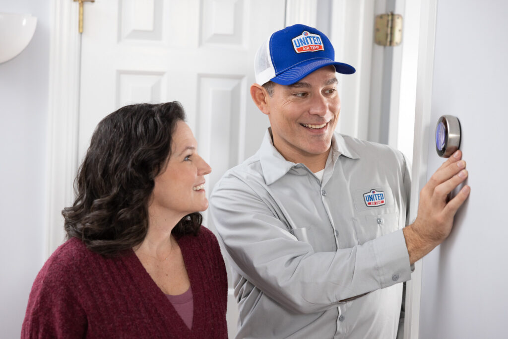 UAT technician showing a homeowner how to adjust her new smart thermostat on a white wall.