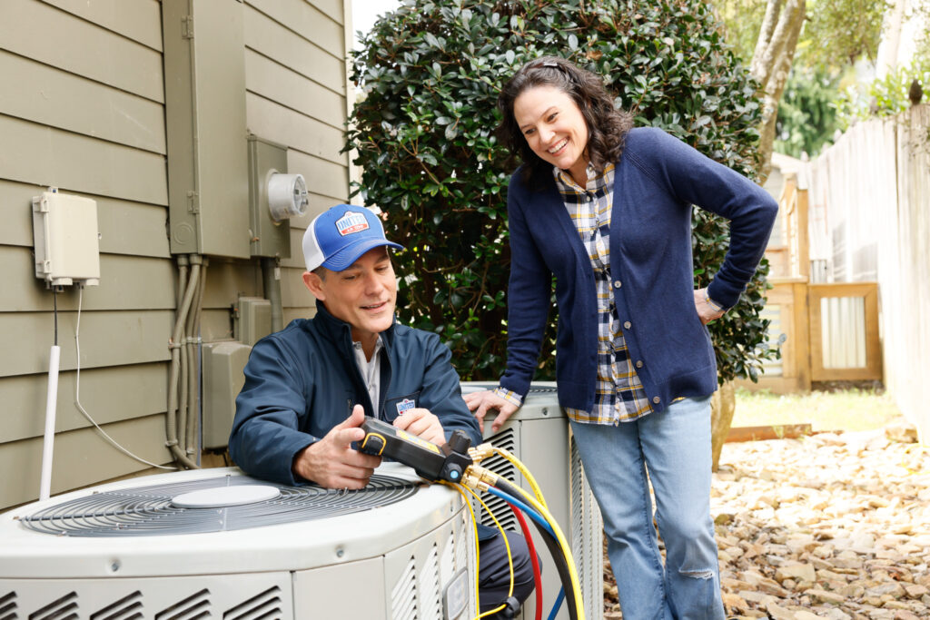 HVAC technician servicing AC unit while talking to a homeowner