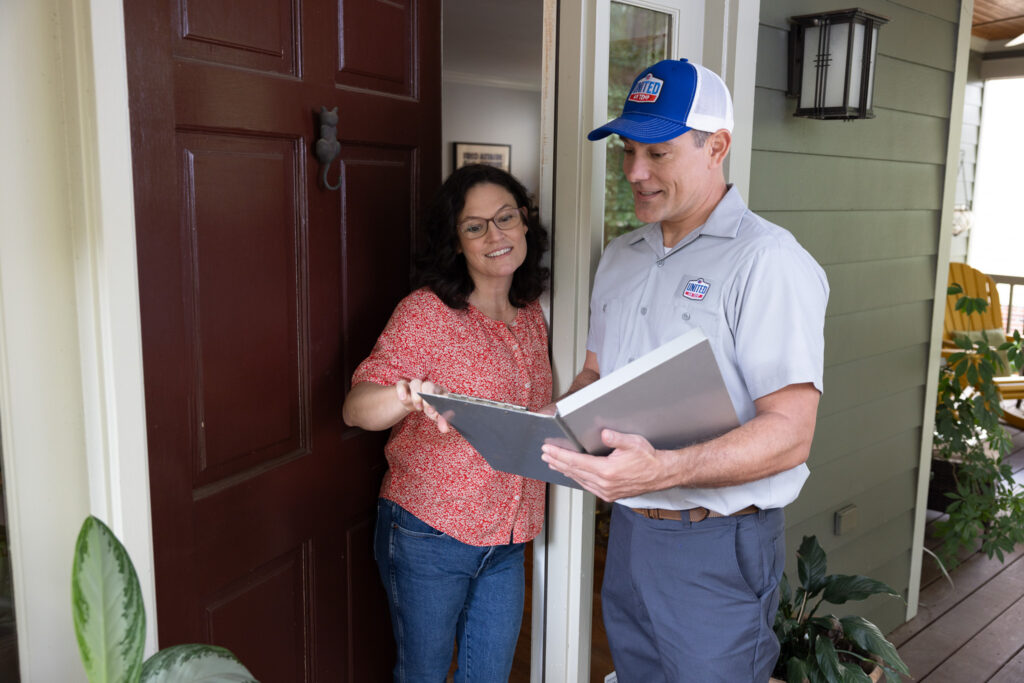 UAT technician talking to a homeowner at her front door and looking at a folder together.