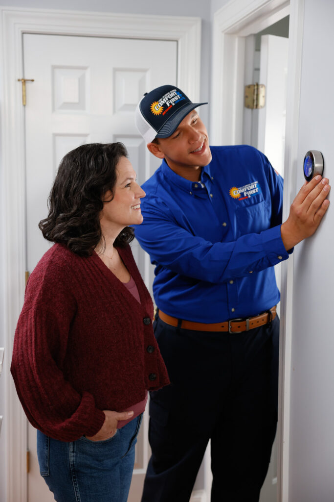 Technician showing homeowner new features on her smart thermostat on a white wall in a hallway.