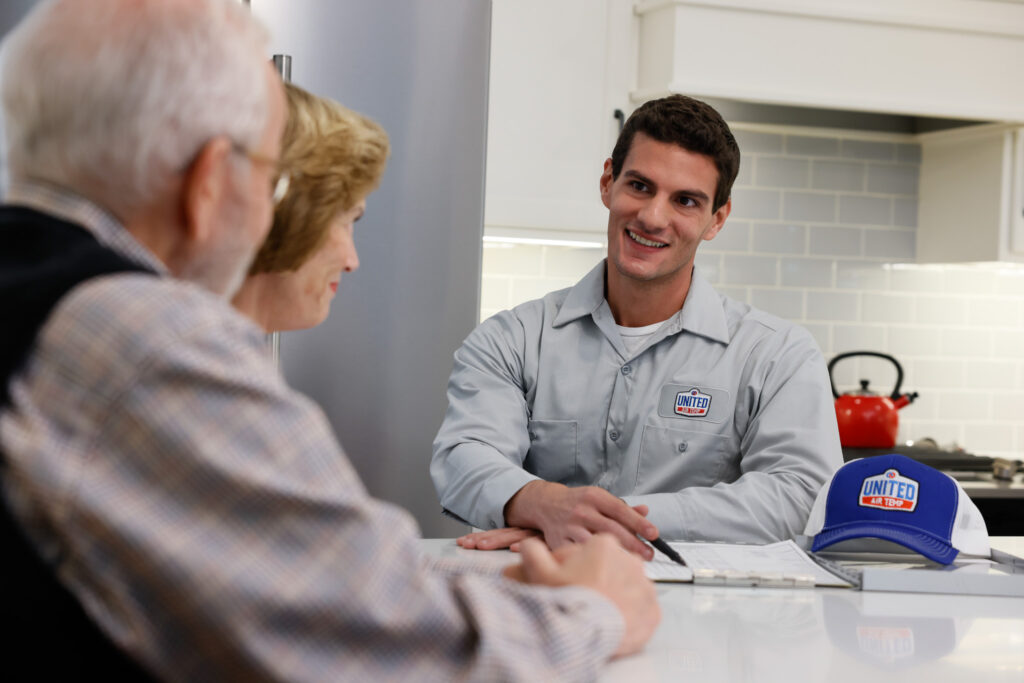 UAT technician speaking with two homeowners at their kitchen counter.