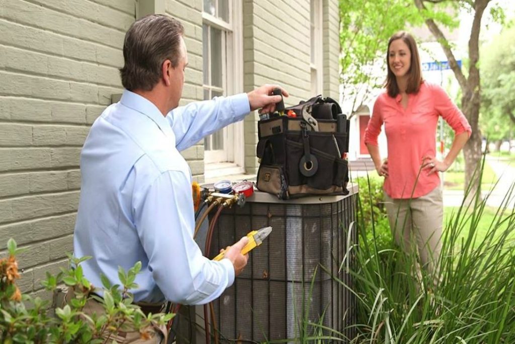 HVAC technician maintaining AC unit while talking to the homeowner