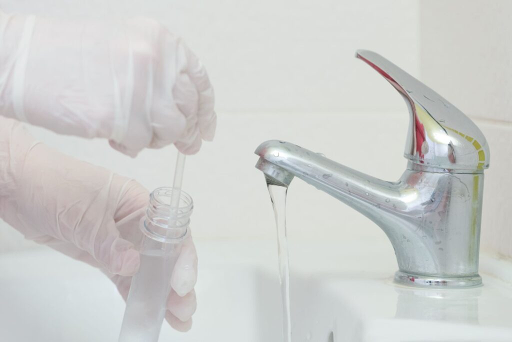 Gloved hands taking a water quality sample from a sink faucet