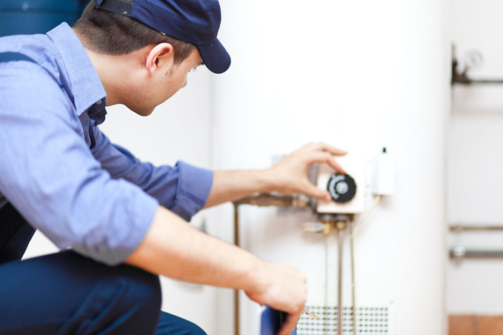 plumber adjusting water heater temperature on a white tank model.